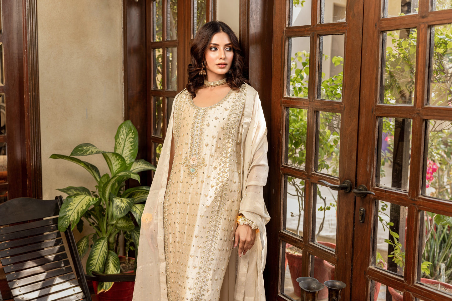 Woman in a white traditional formal shirt outfit standing in a room with wooden doors and plants.