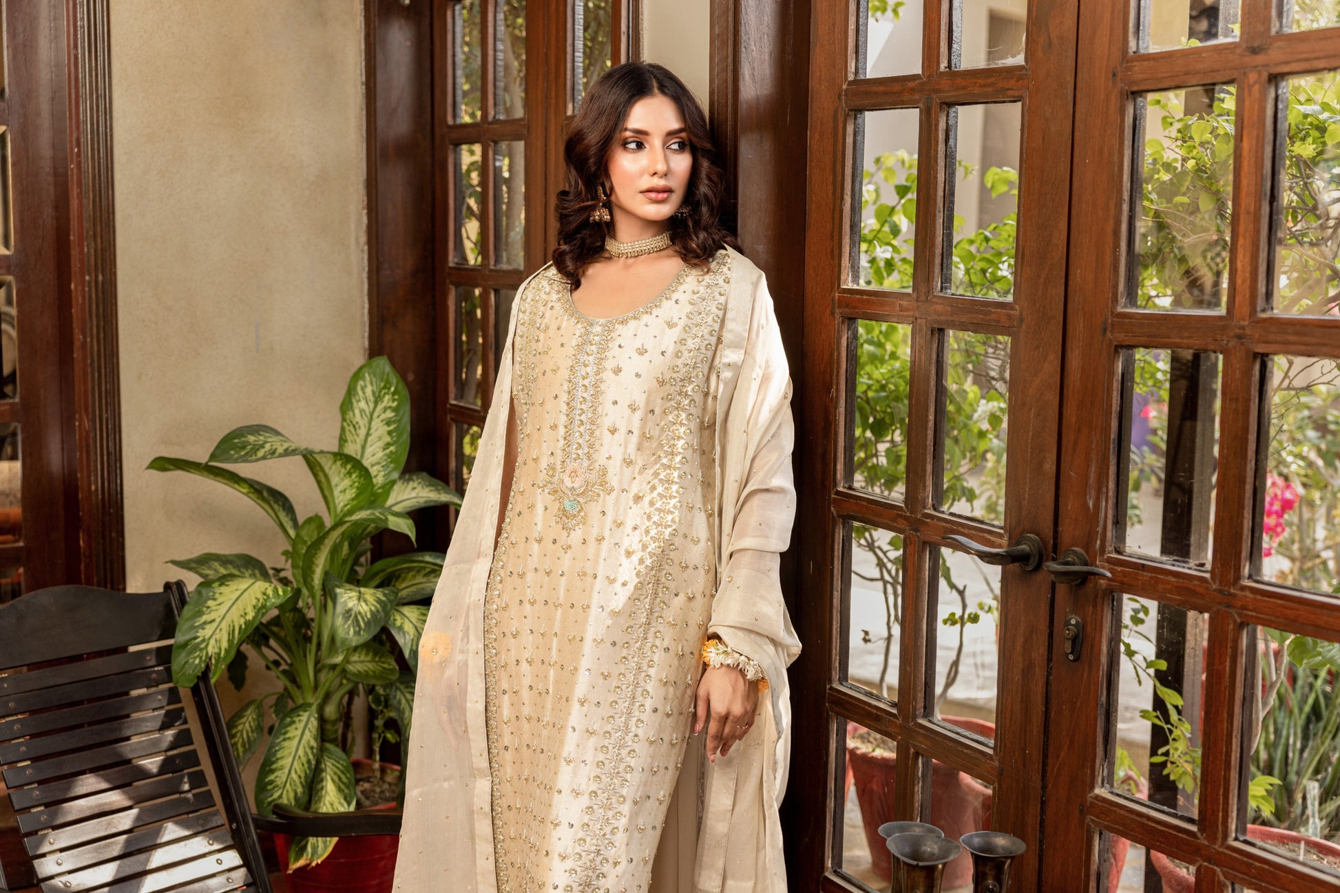 Woman in a white traditional formal shirt outfit standing in a room with wooden doors and plants.