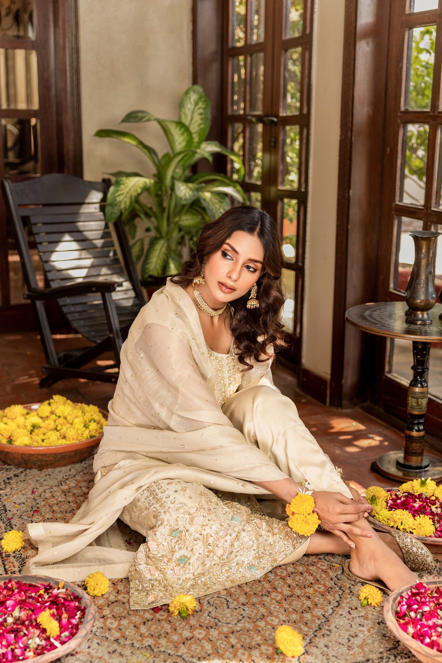 Woman in traditional formal shirt attire sitting on the floor with floral decorations around her.