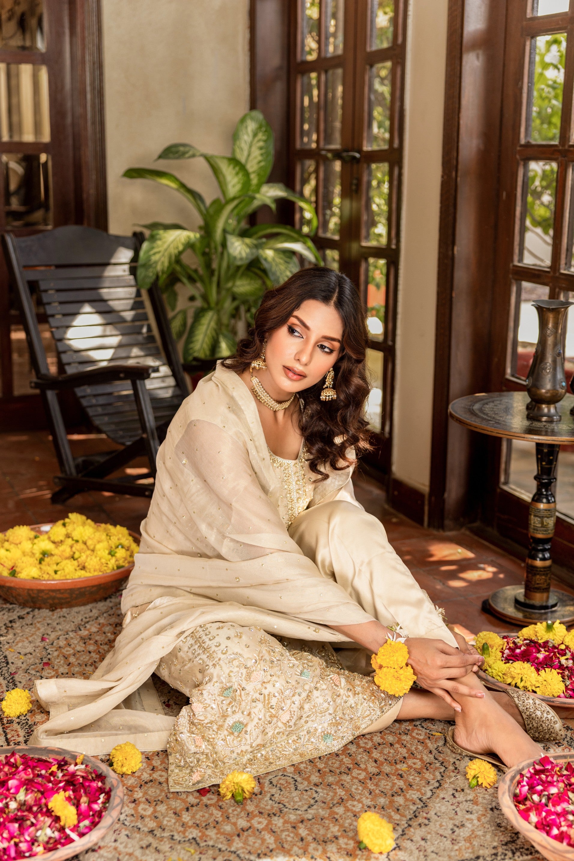 Woman in traditional formal shirt attire sitting on the floor with floral decorations around her.