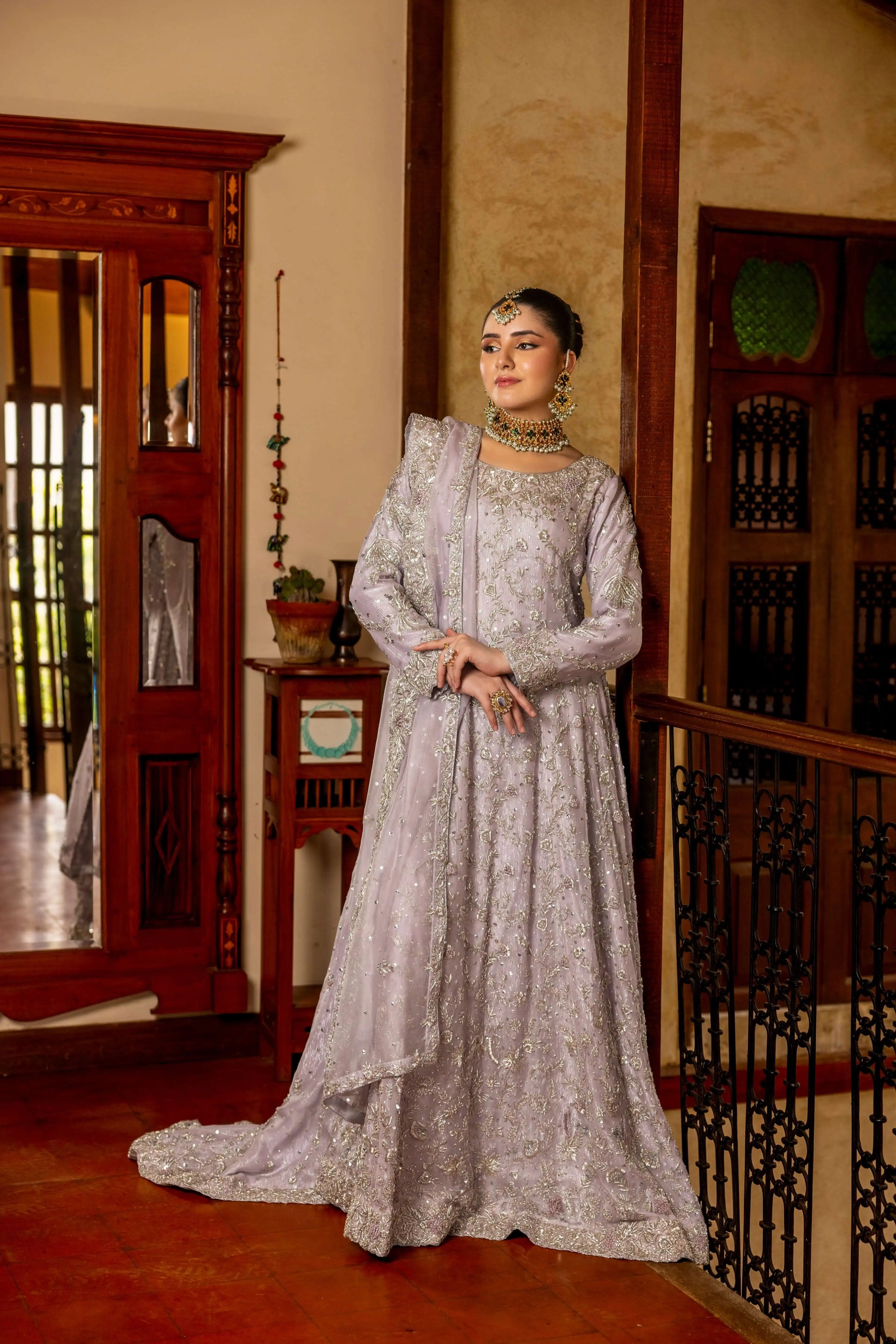 Woman in a silver embroidered dress standing in an indoor setting with wooden furniture.
