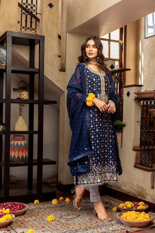 Woman in a blue traditional formal outfit standing in an indoor setting with decorative elements.
