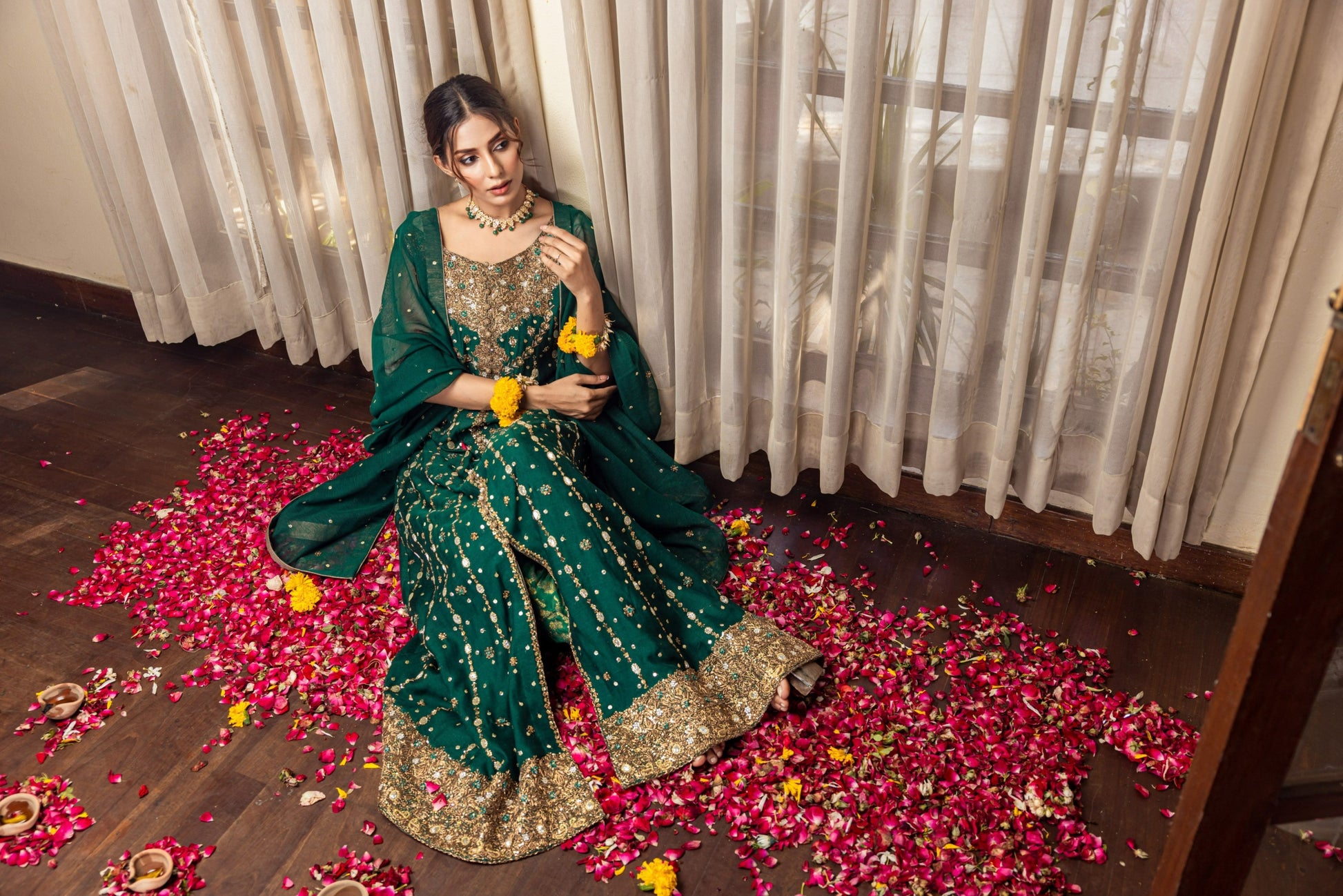 Woman in a green traditional front-open maxi outfit sitting on a floor with rose petals