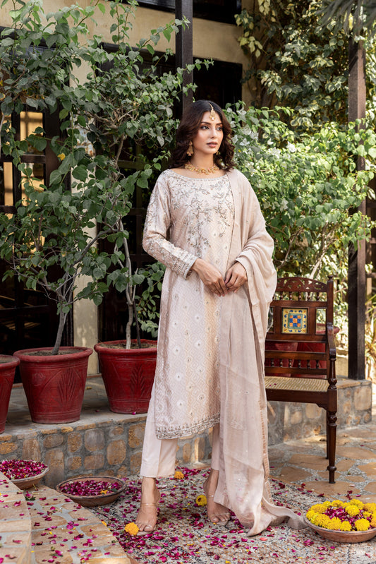 Woman in a beige embroidered formal basic shirt outfit standing in a garden setting with potted plants and a chair.