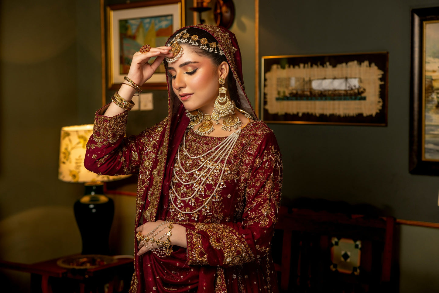 Woman in traditional bridal sharara red and gold embroidered outfit with jewelry indoors.