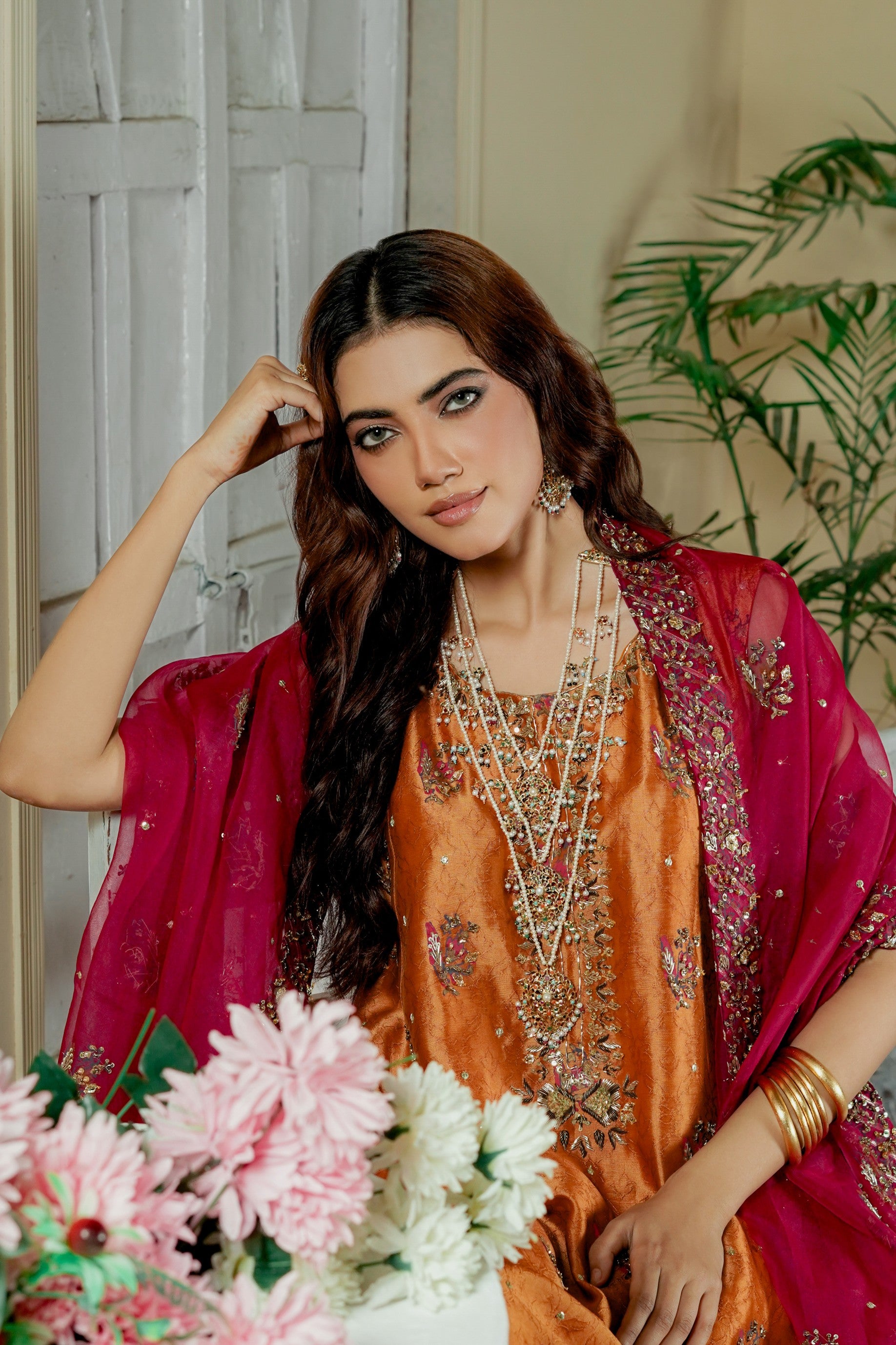 Woman in traditional formal wear maxi outfit with jewelry and flowers, indoor setting