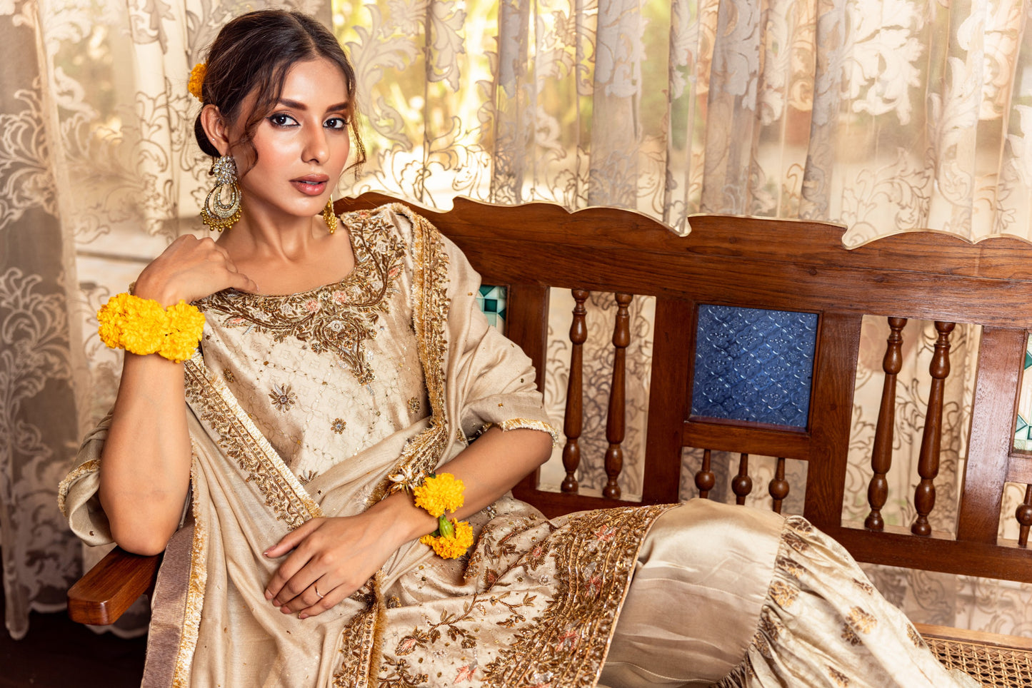 Woman in a traditional Party Wear Garara with floral decorations sitting on a wooden bench.