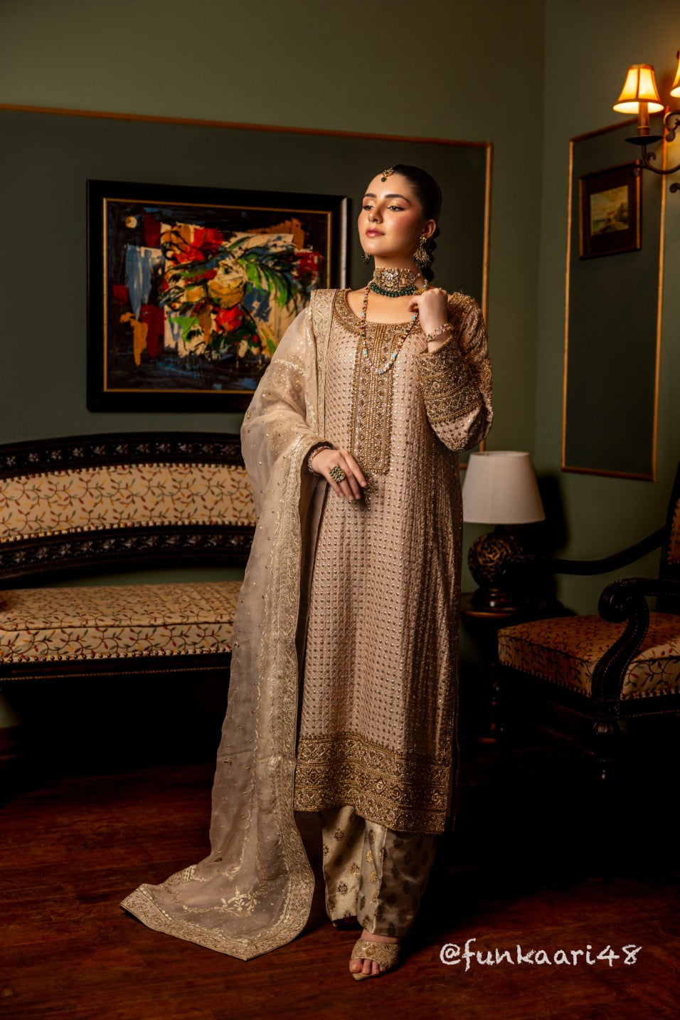 Woman in traditional wedding formal shirt outfit standing in a decorated room with a lamp and sofa.