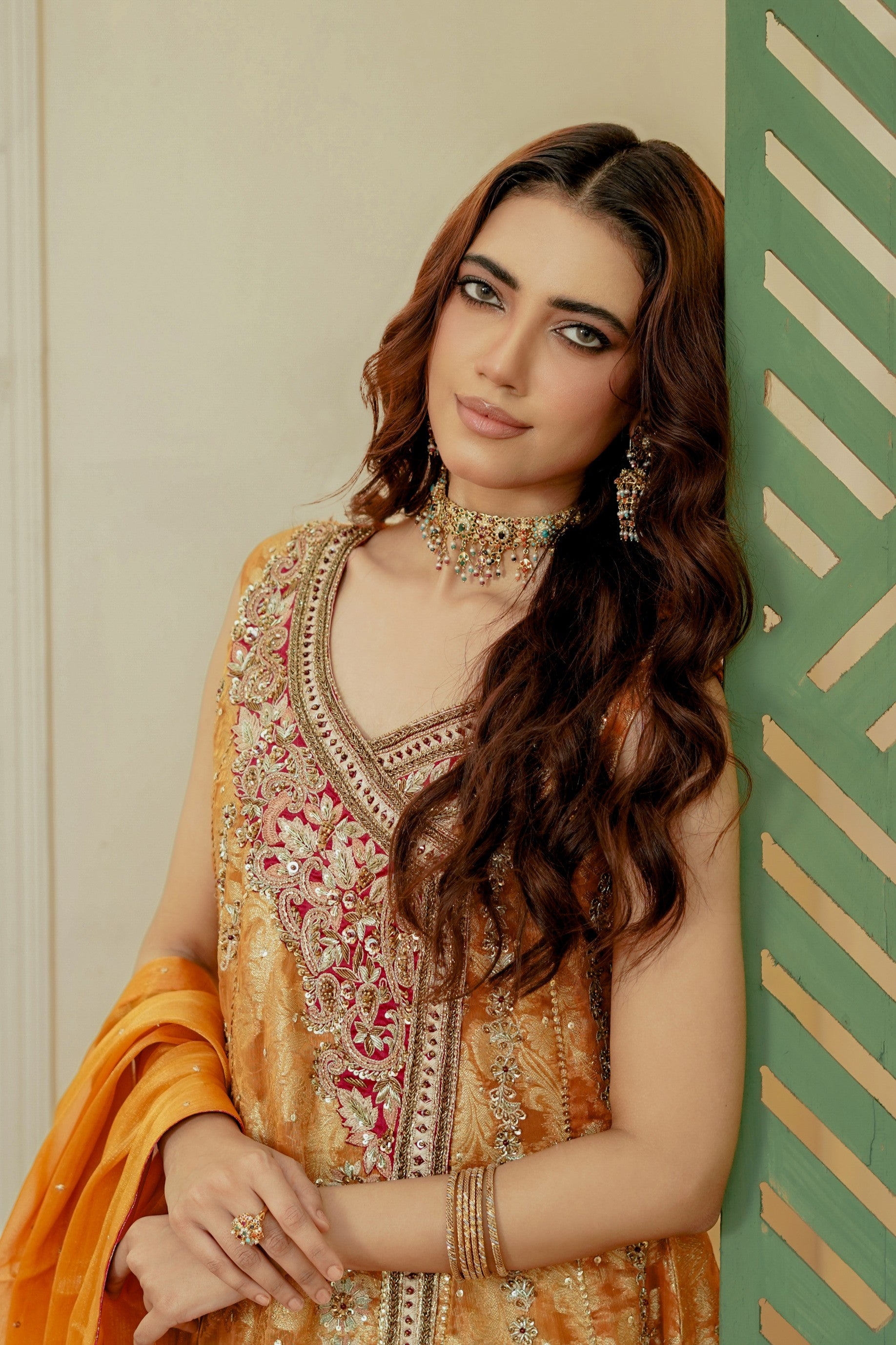 Woman in traditional embroidered outfit with jewelry against a green and beige background