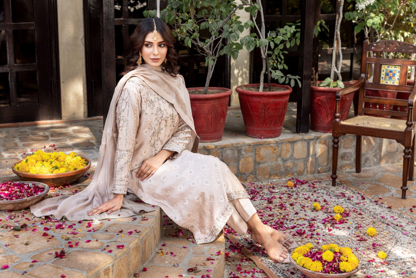 Woman in traditional formal basic shirt attire sitting on a stone step with flowers and plants around