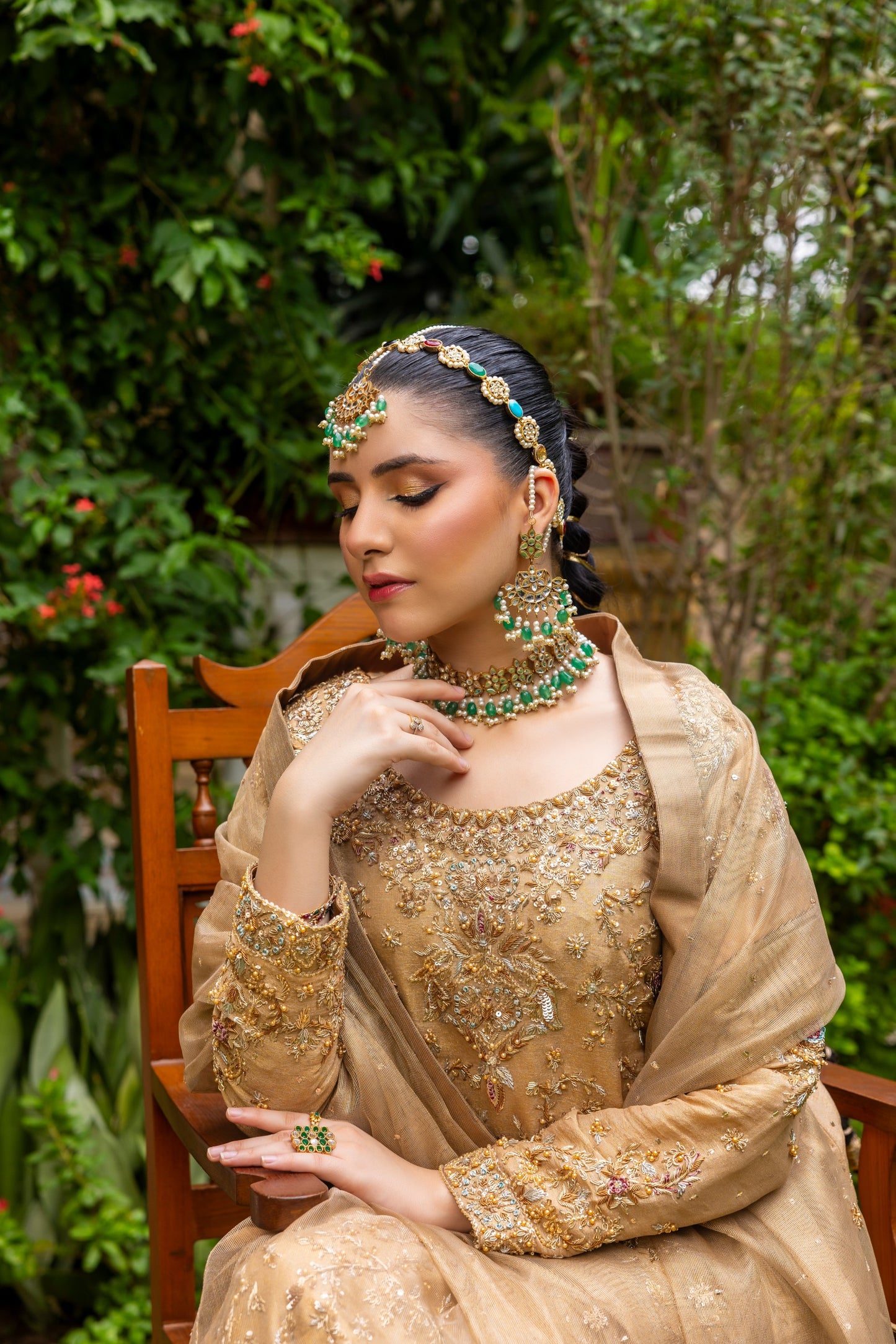 Woman in traditional beige embroidered party wear shirt with jewelry sitting outdoors.