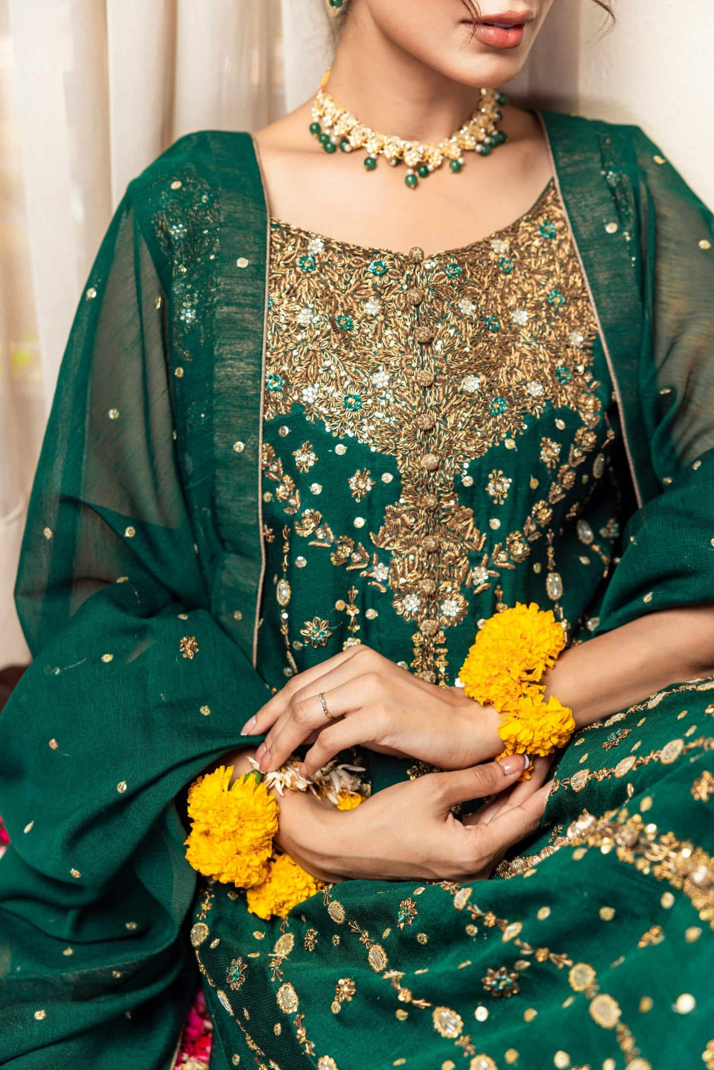 Person wearing a green and gold traditional front-open maxi outfit with jewelry and yellow flowers.