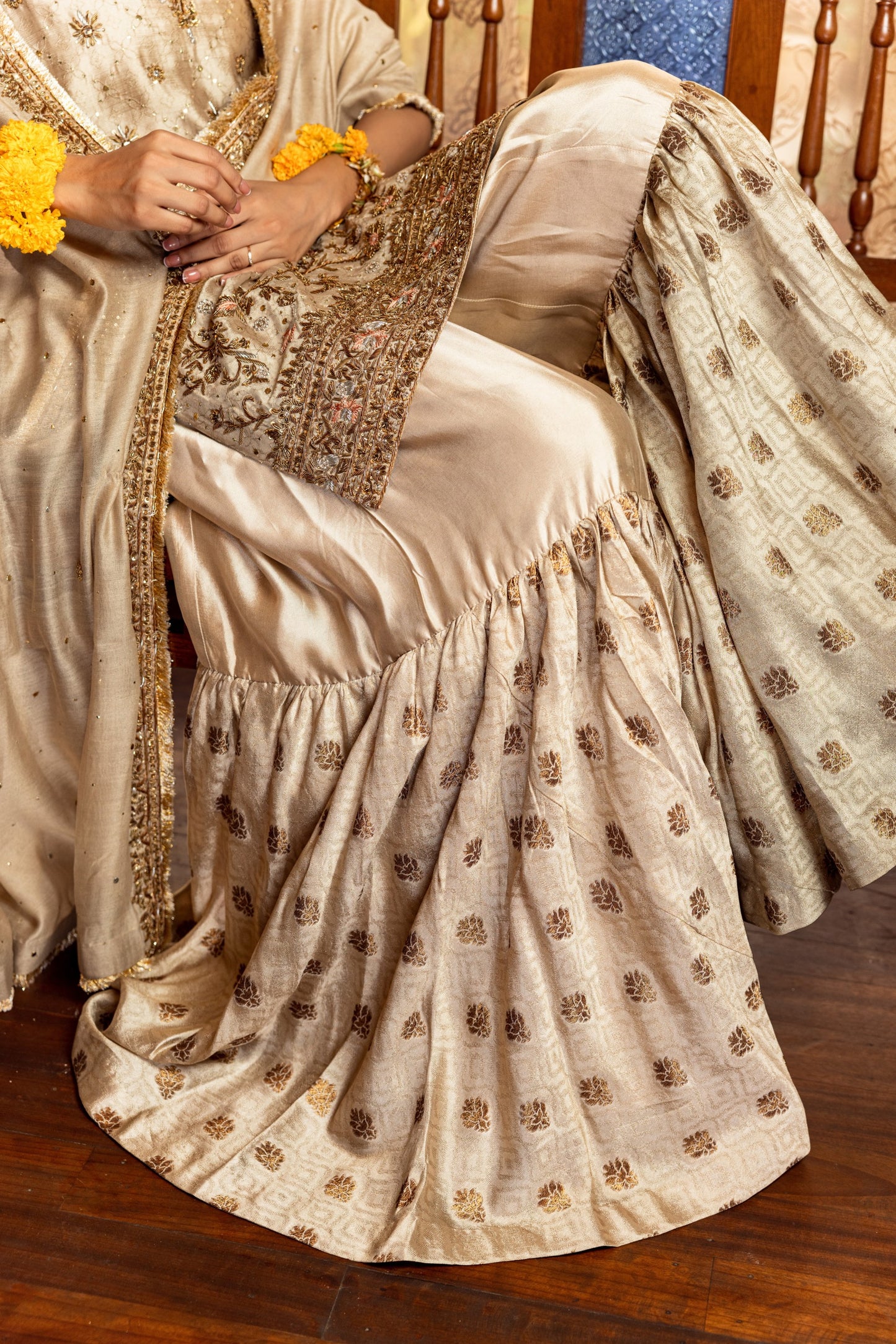 Person wearing a traditional beige Party Wear Garara with gold patterns on a wooden floor.