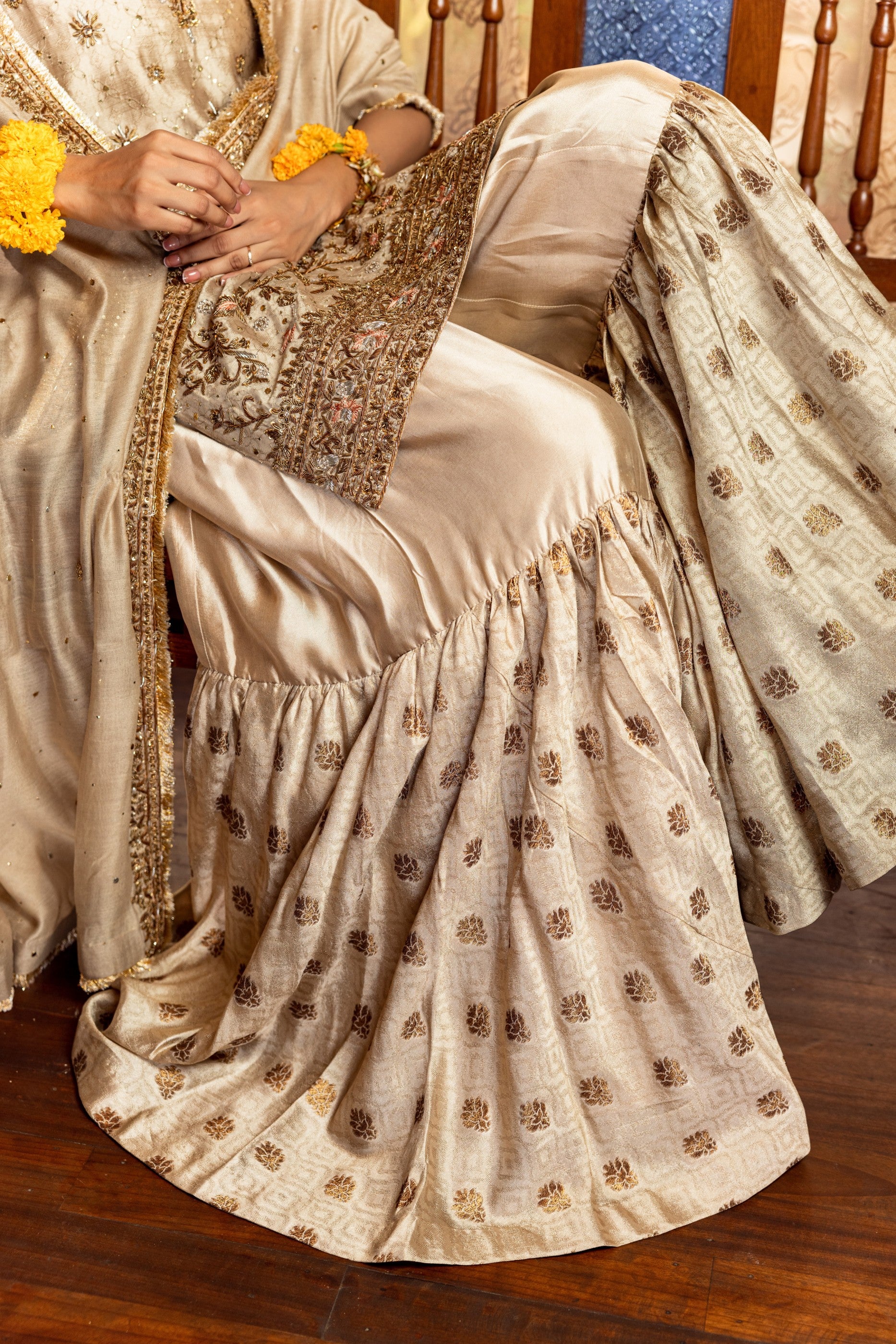 Person wearing a traditional beige Party Wear Garara with gold patterns on a wooden floor.