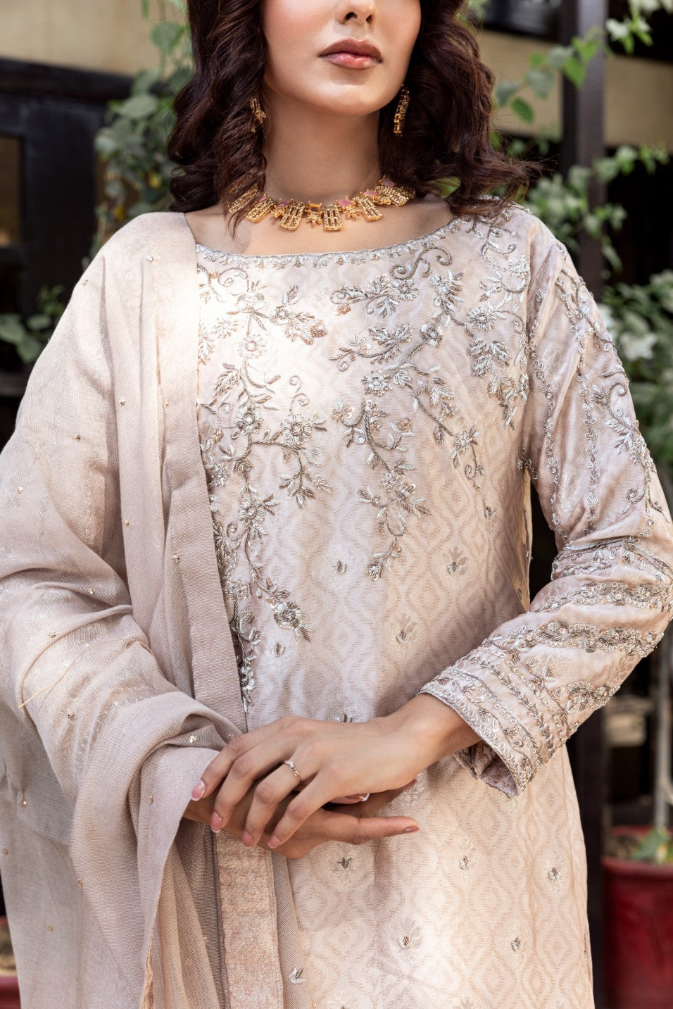 Woman wearing a beige embroidered traditional formal basic shirt outfit with a gold necklace.