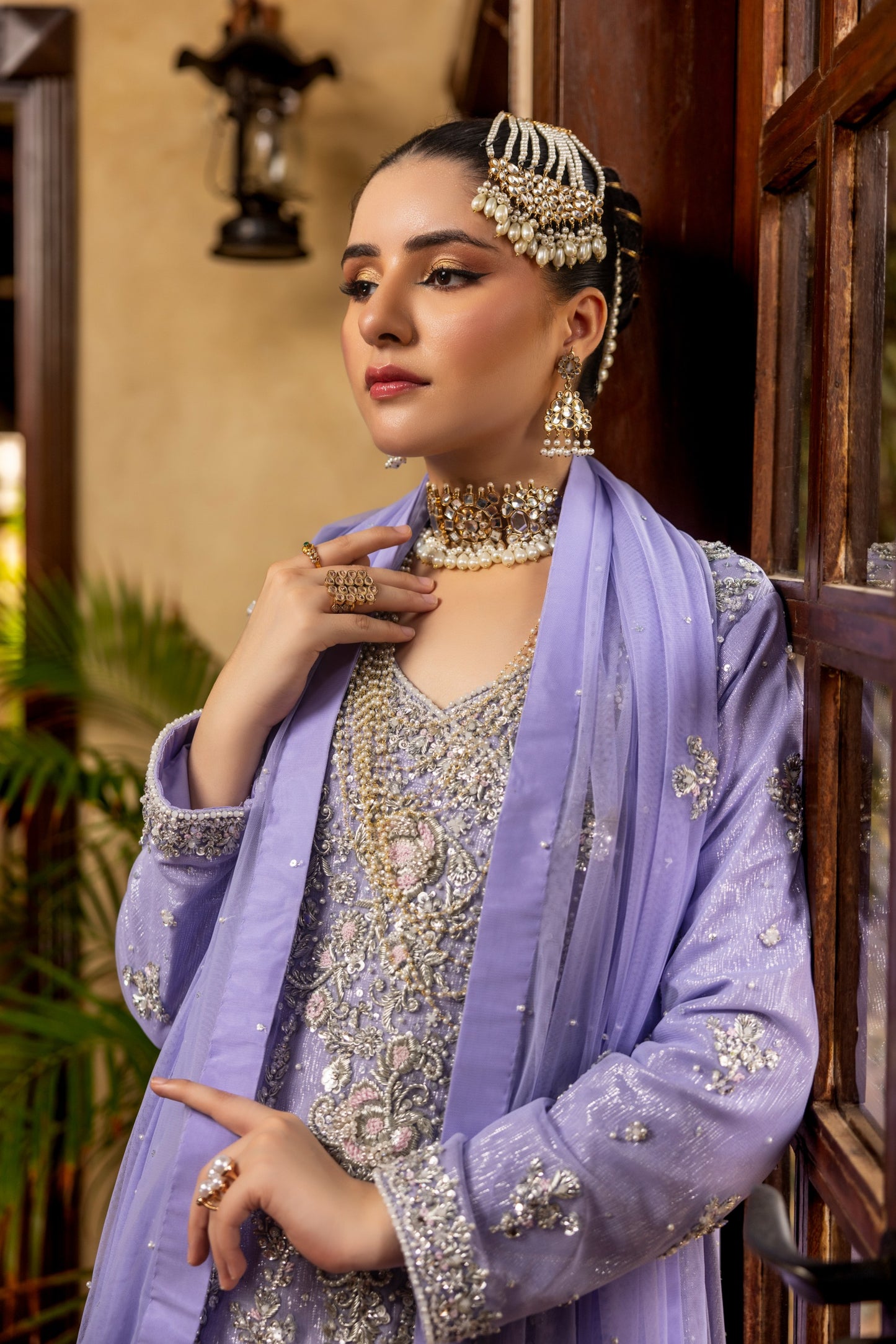 Woman in traditional bridal maxi attire with jewelry, standing indoors.