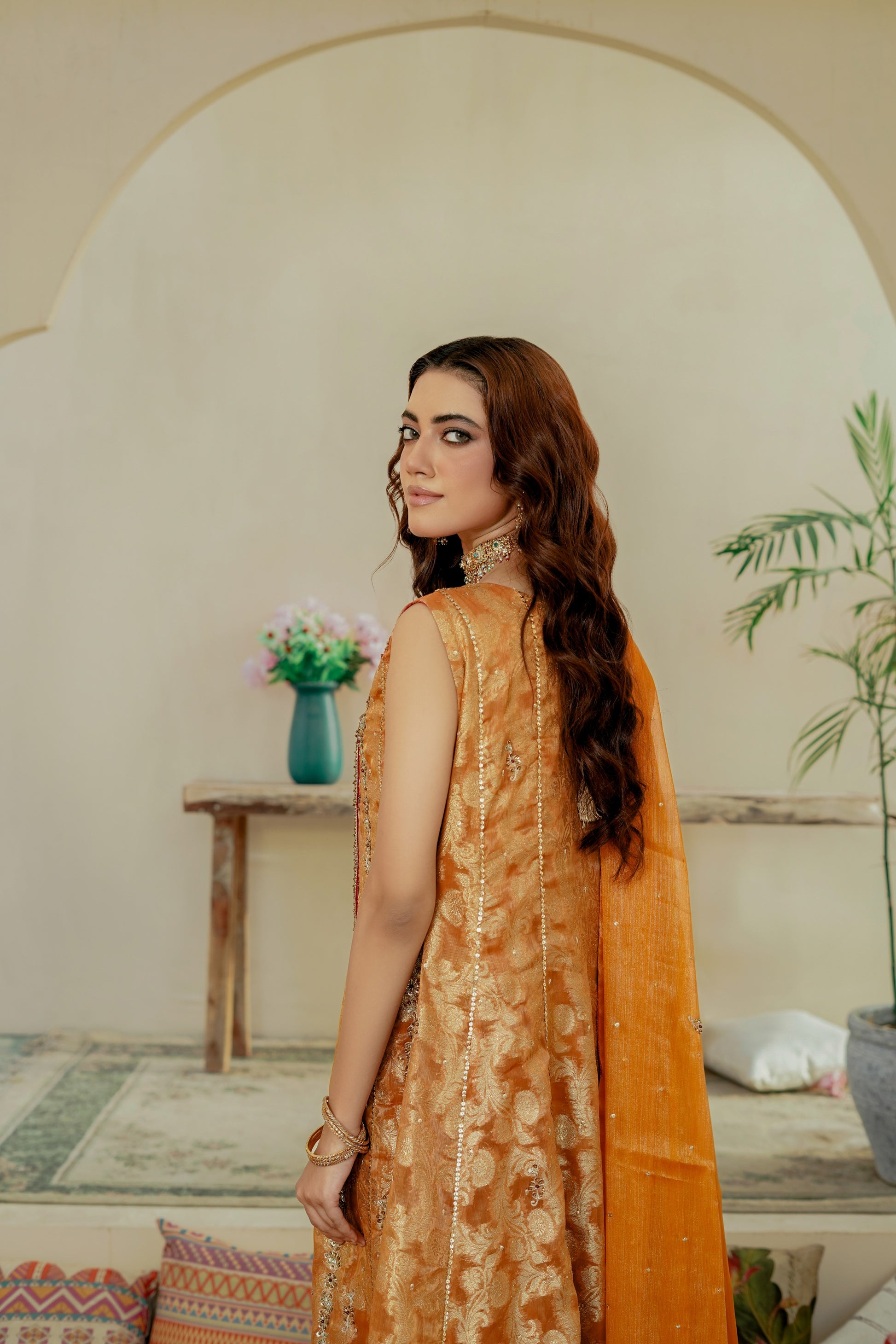 Woman in an orange traditional formal frock outfit standing in a room with decor elements.
