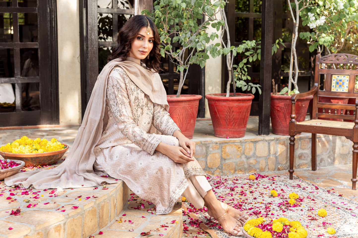 Woman in traditional formal basic shirt attire sitting on a stone step with flowers and potted plants in the background