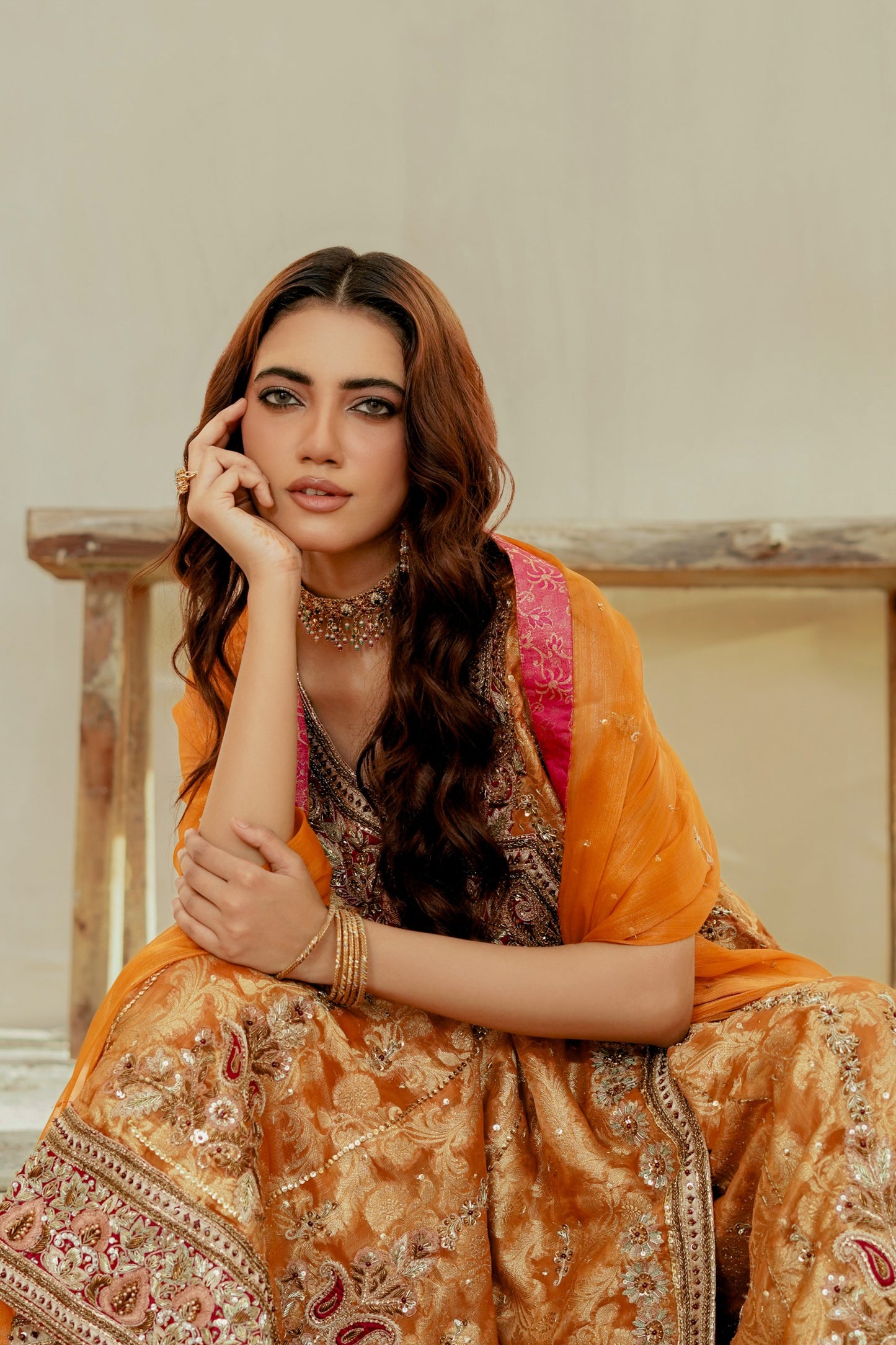 Woman in traditional orange and pink formal frock outfit sitting on a wooden bench.