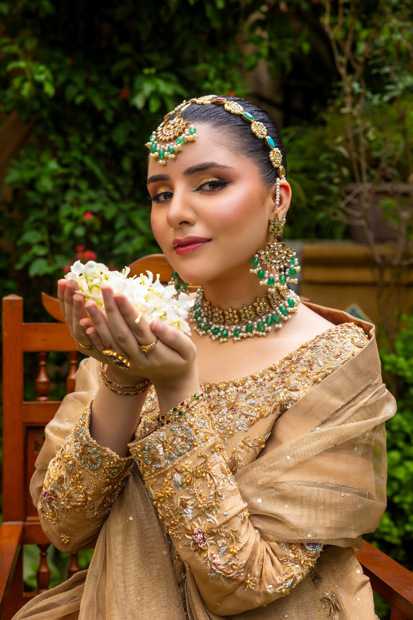 Woman in traditional party wear shirt attire with jewelry and a bowl of flowers, seated outdoors.