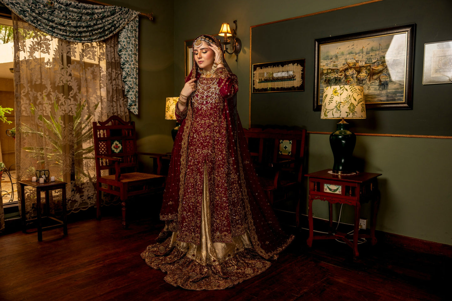 Woman in a traditional bridal sharara embroidered dress standing in an ornate room with decorative elements.