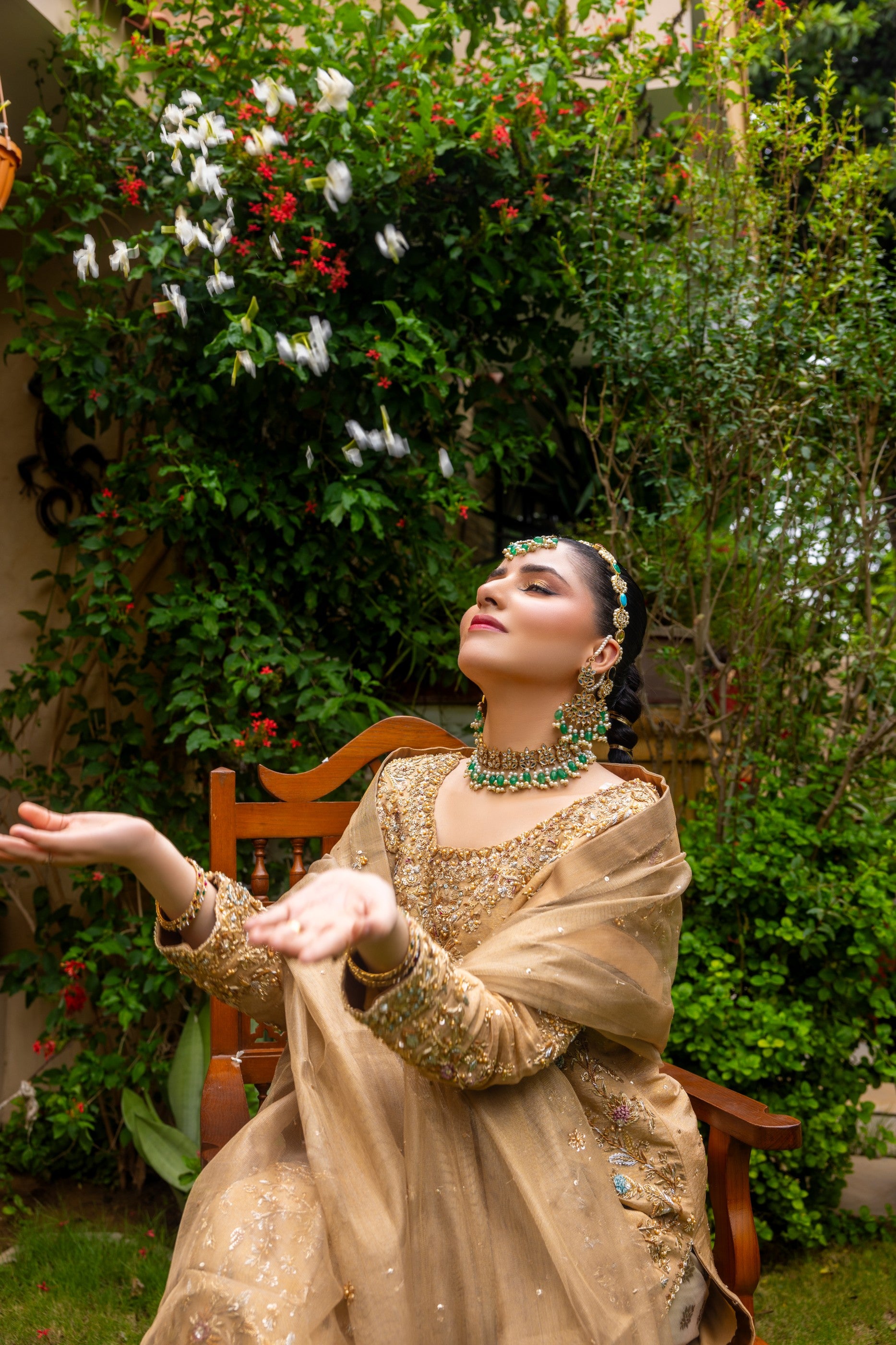 Woman in traditional attire sitting outdoors with greenery and flowers in the background