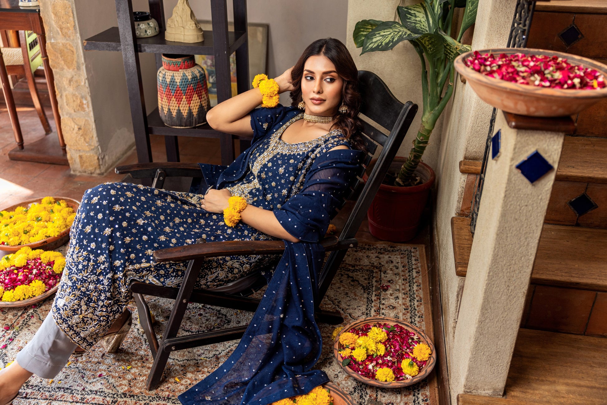 Woman in a blue traditional formal  outfit sitting on a chair with decorative items around her.
