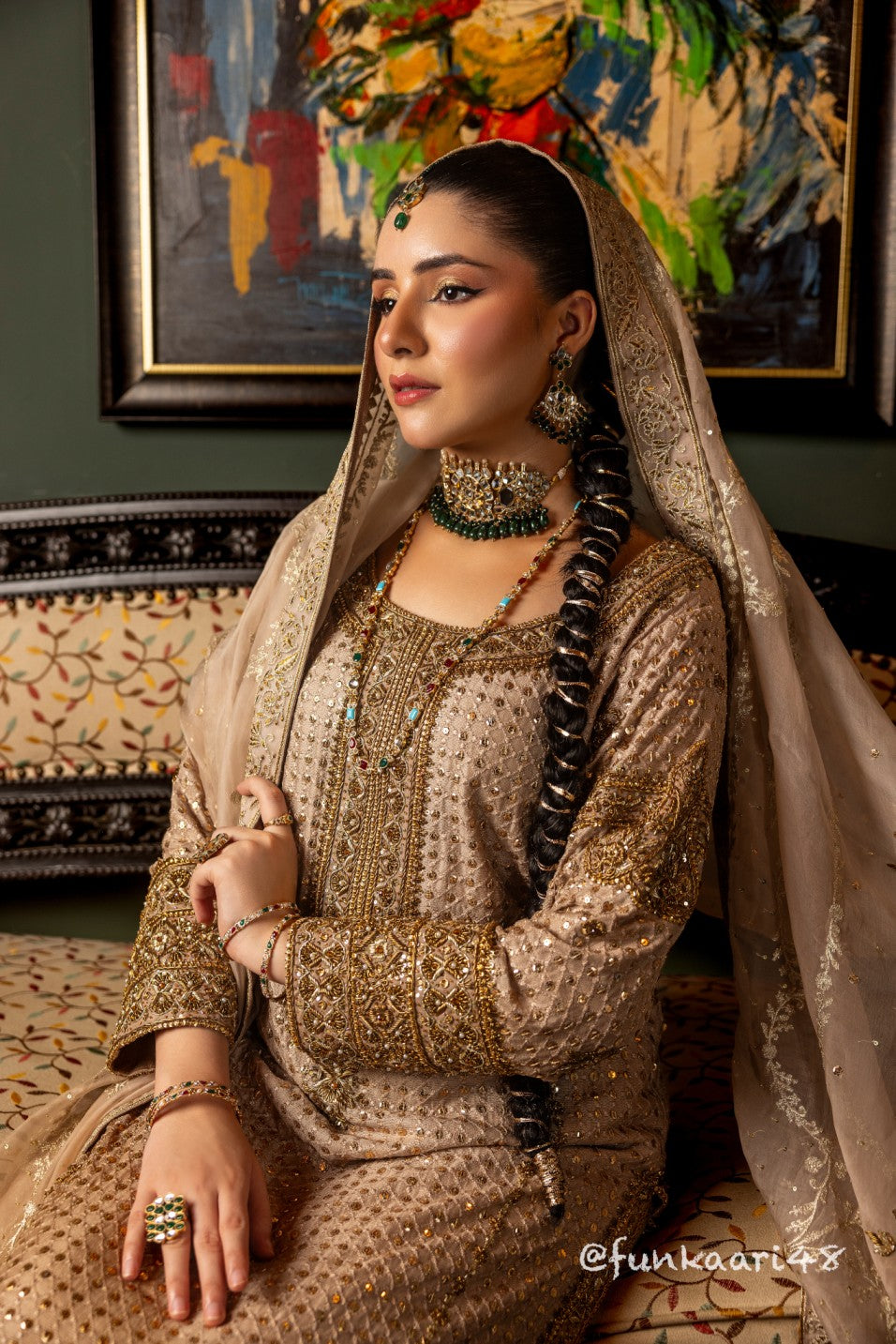 Woman in traditional attire with jewelry, sitting in a decorated room.