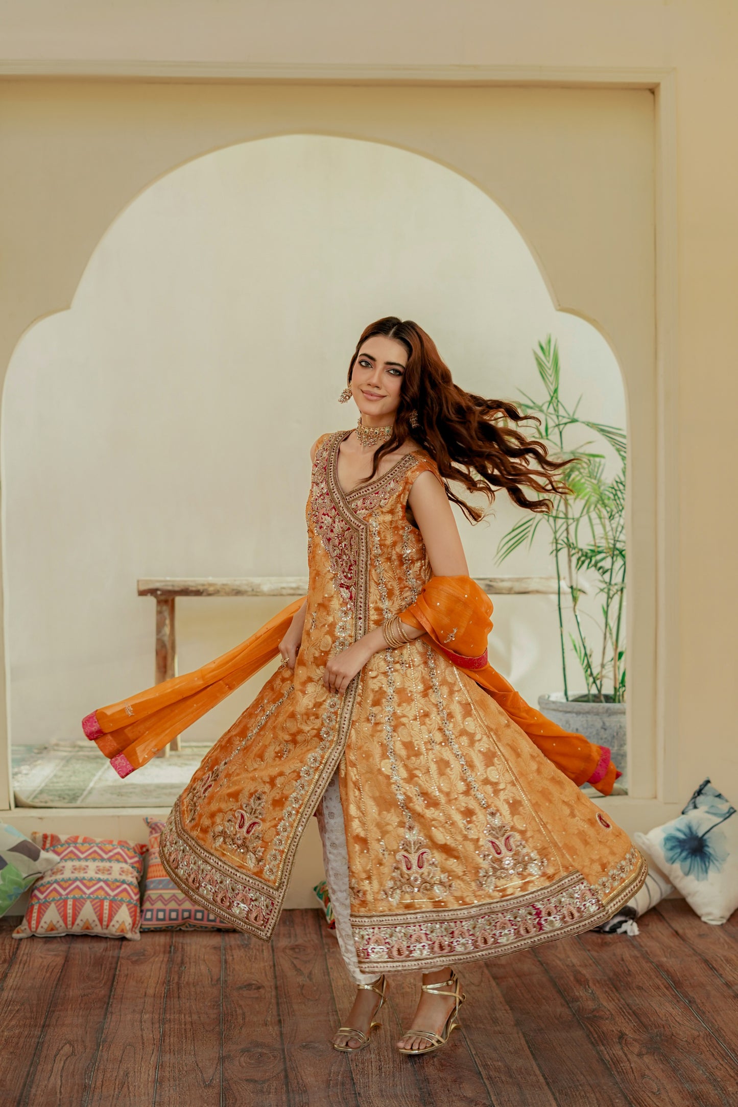 Woman in a traditional formal frock outfit with orange and yellow colors standing indoors.