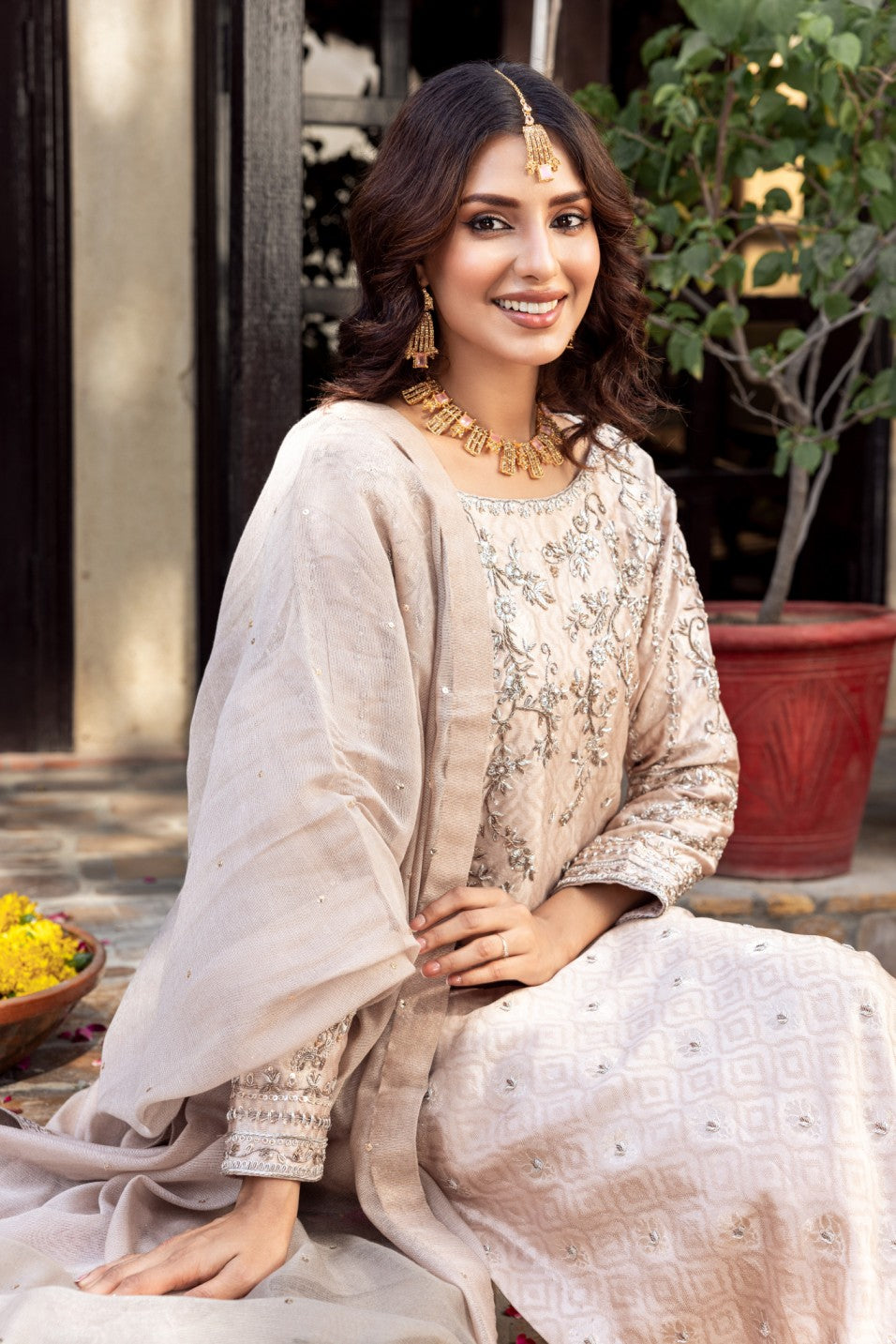 Woman in traditional formal basic shirt attire sitting outdoors with plants in the background