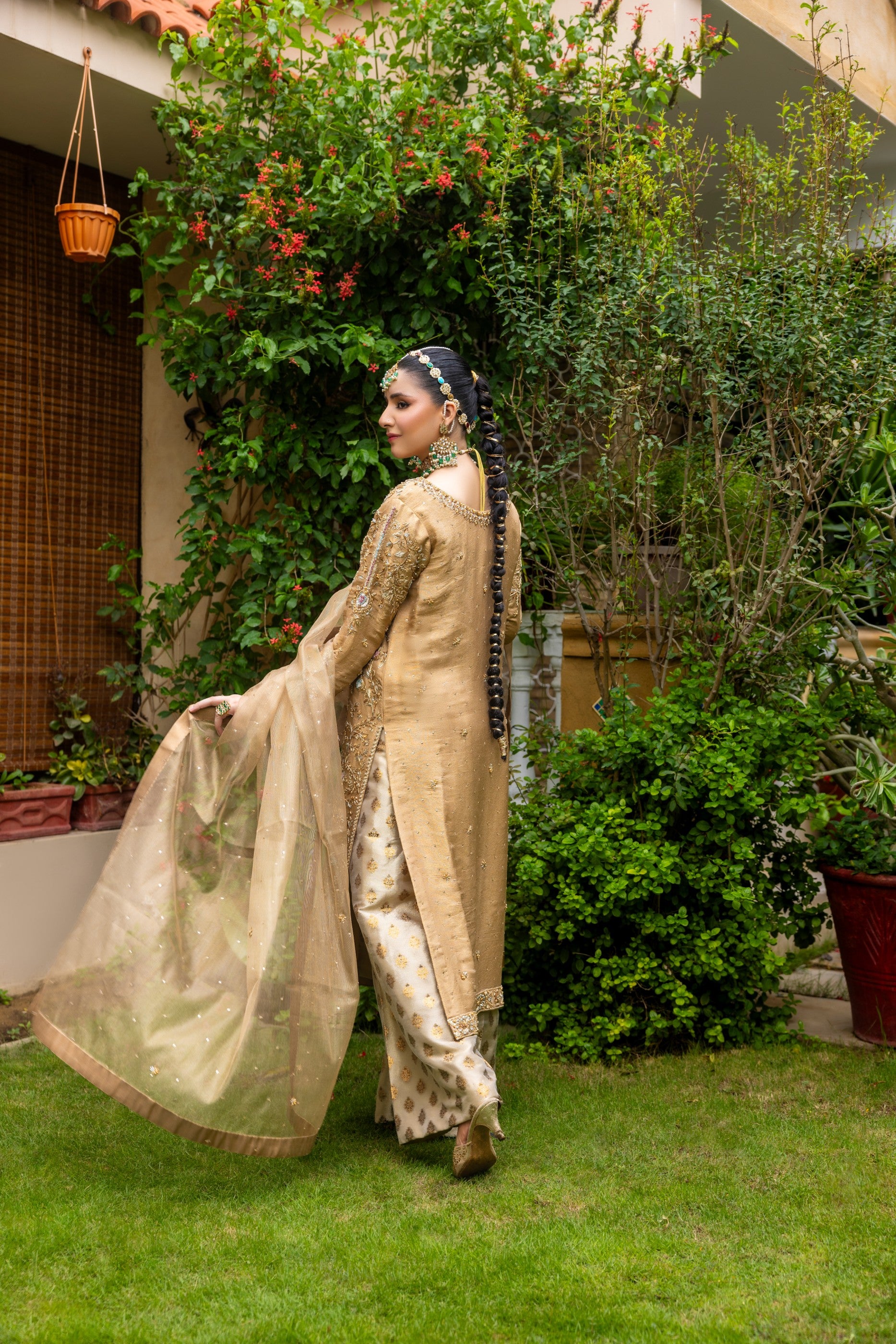 Woman in traditional party wear shirt attire standing in a garden with greenery and a building in the background