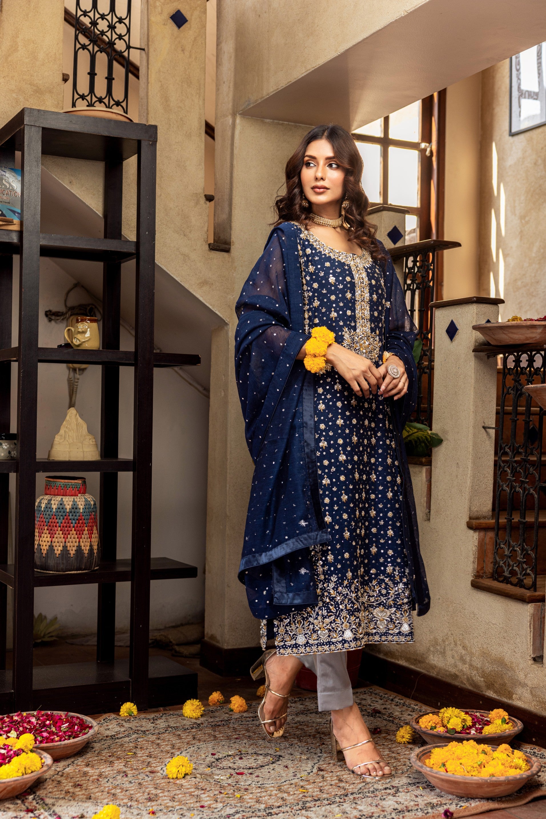 Woman in a blue traditional formal outfit standing in an indoor setting with decorative elements.