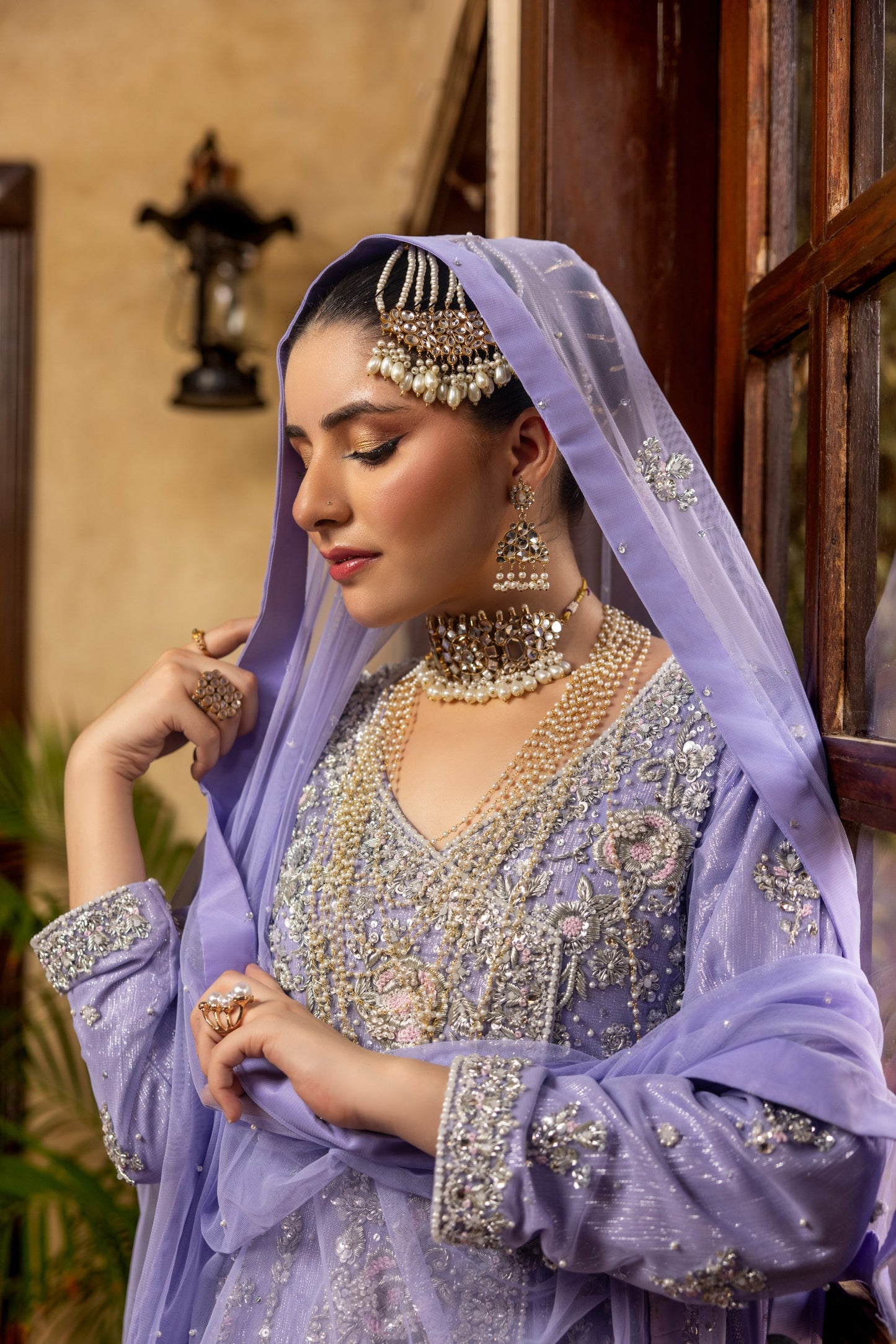 Woman in a traditional lavender bridal maxi outfit with intricate jewelry indoors.