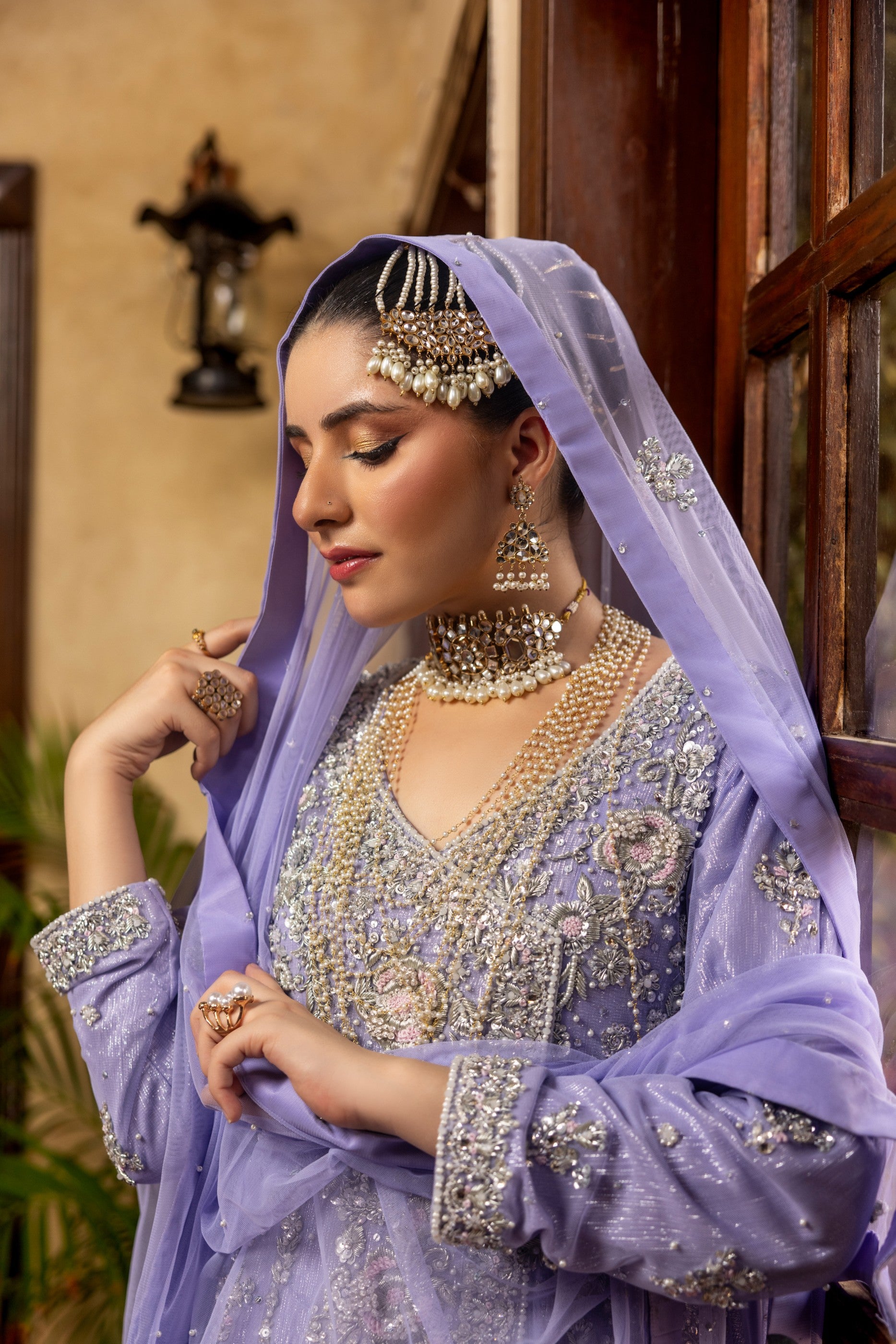 Woman in a traditional lavender bridal maxi outfit with intricate jewelry indoors.