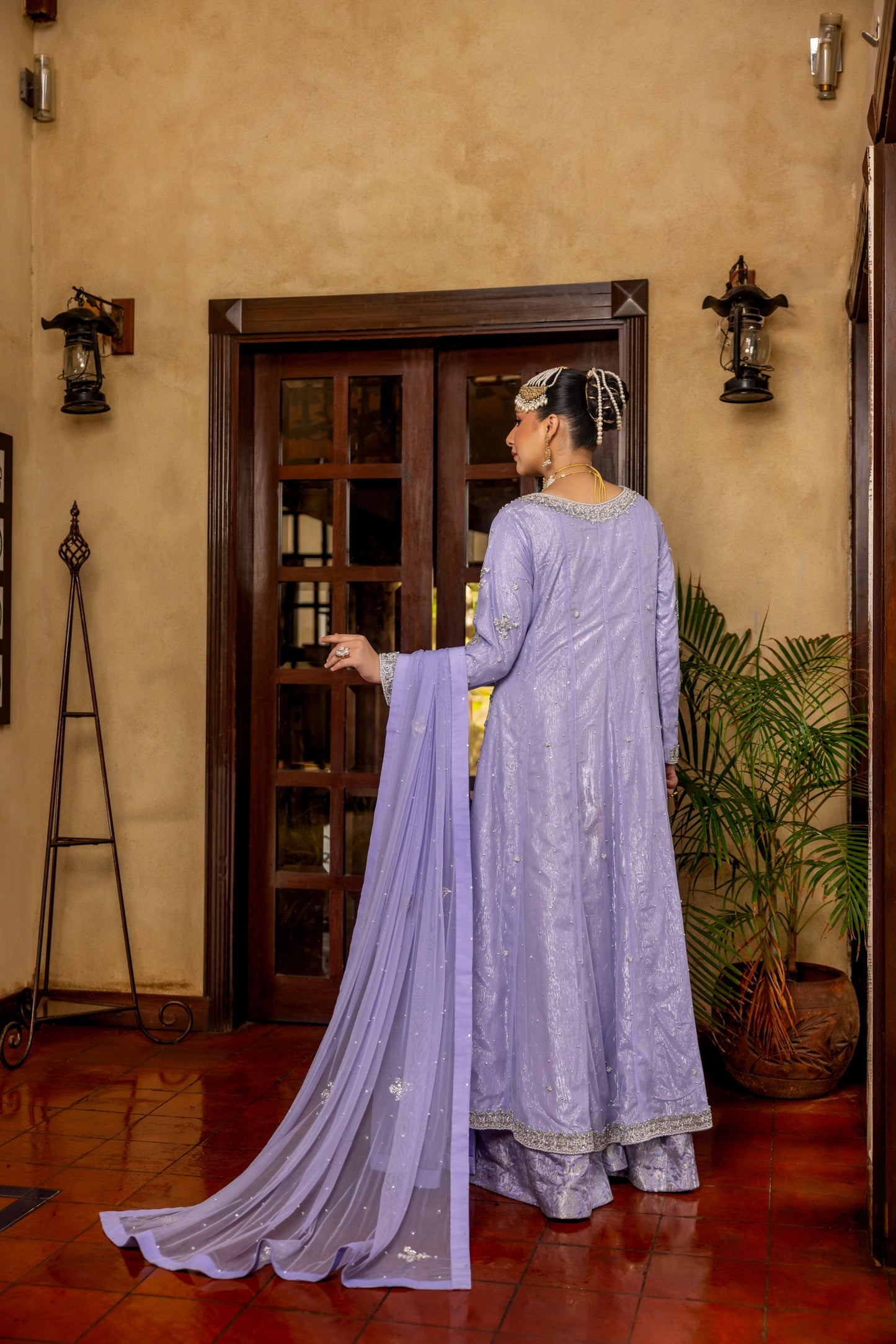 Woman in a lavender traditional bridal maxi outfit standing in a room with wooden floor and wall.
