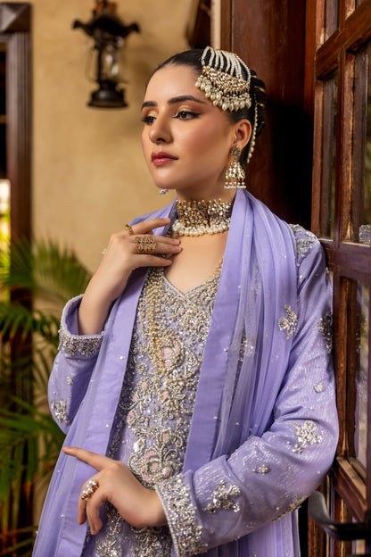 Woman in traditional bridal maxi attire with jewelry, standing indoors.