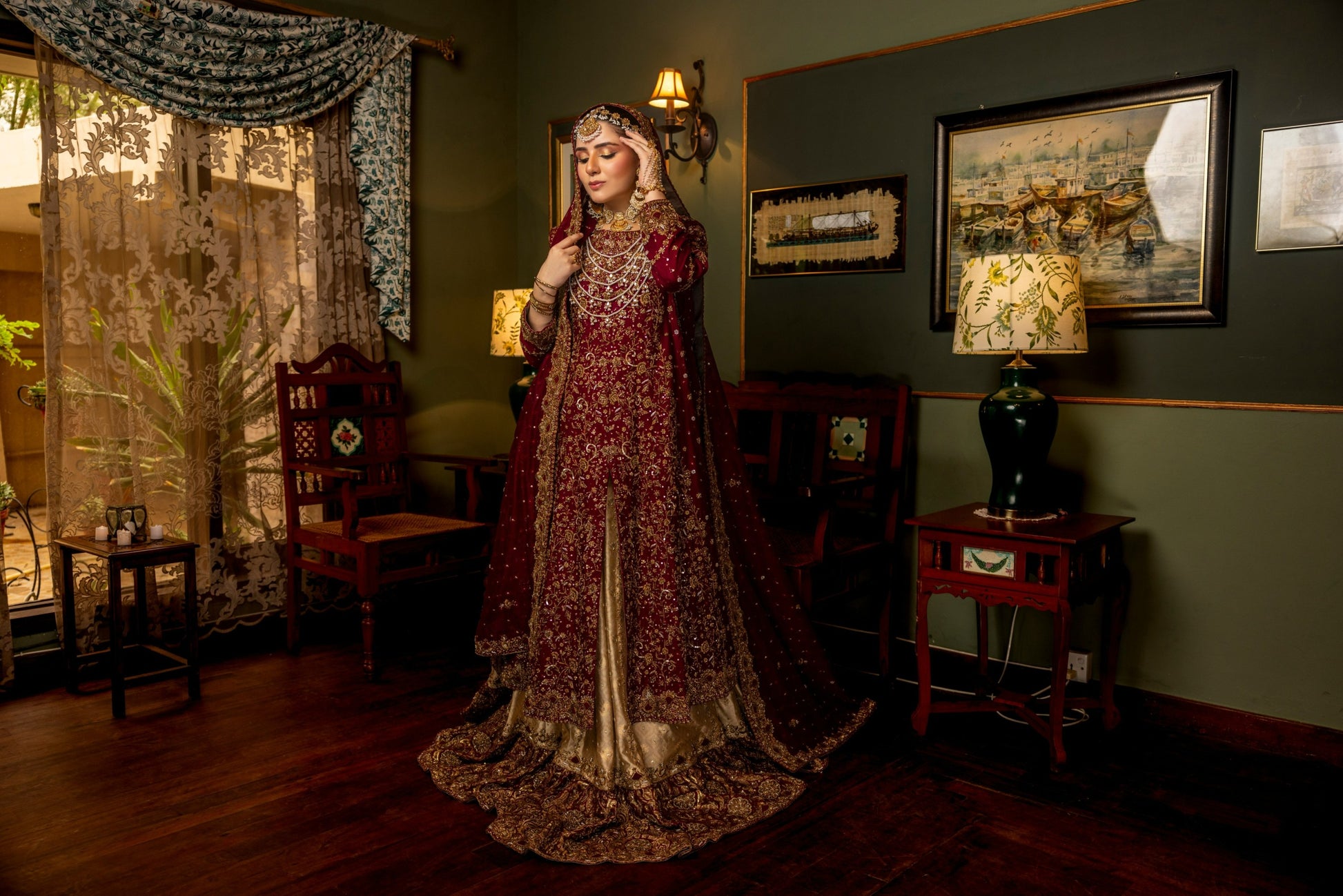 Woman in a traditional bridal sharara embroidered dress standing in an ornate room with decorative elements.