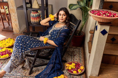 Woman in a blue traditional formal  outfit sitting on a chair with decorative items around her.