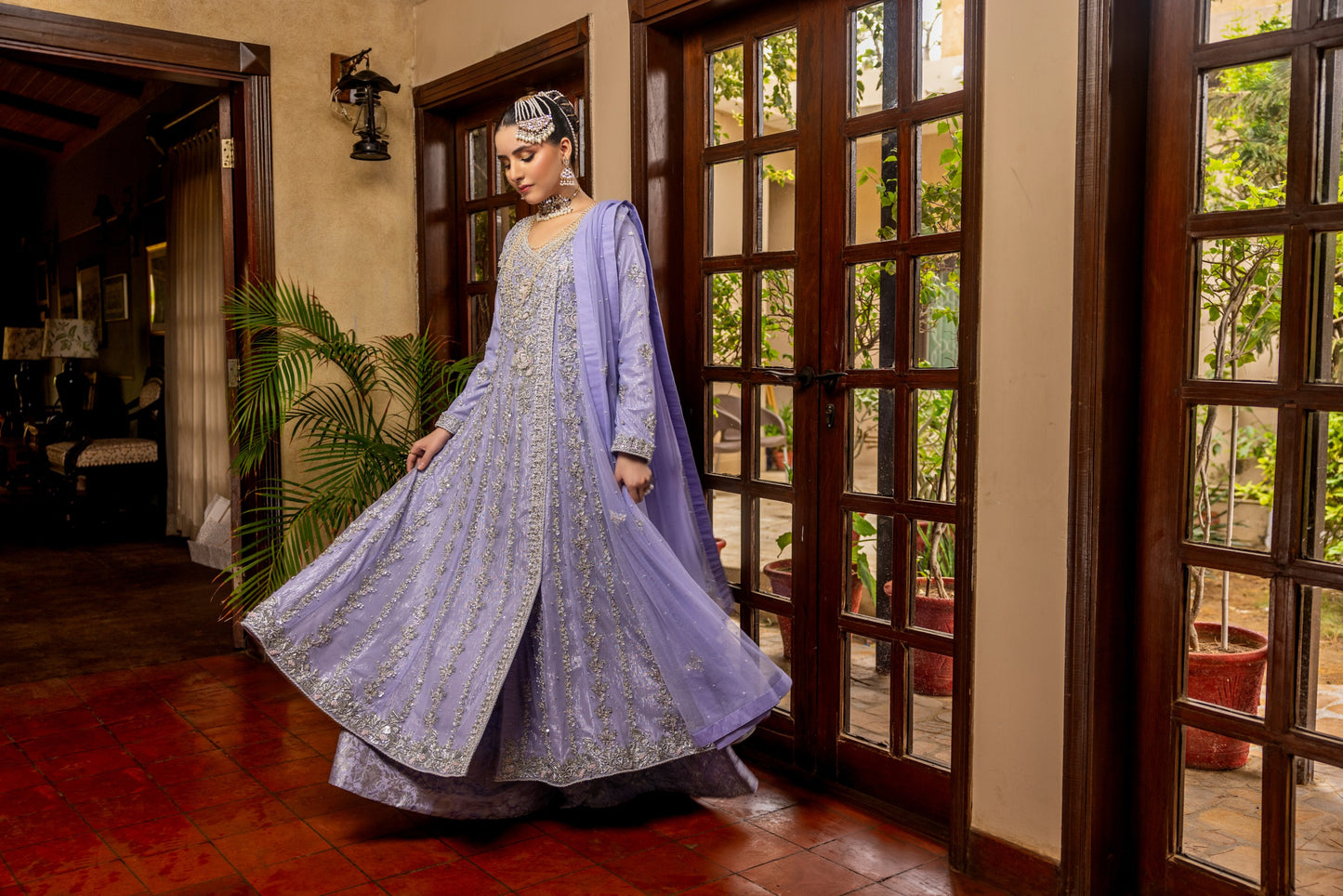 Woman in a light purple traditional bridal maxi outfit standing in a room with wooden floors and large windows.