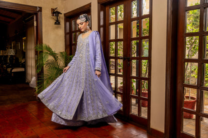 Woman in a light purple traditional bridal maxi outfit standing in a room with wooden floors and large windows.