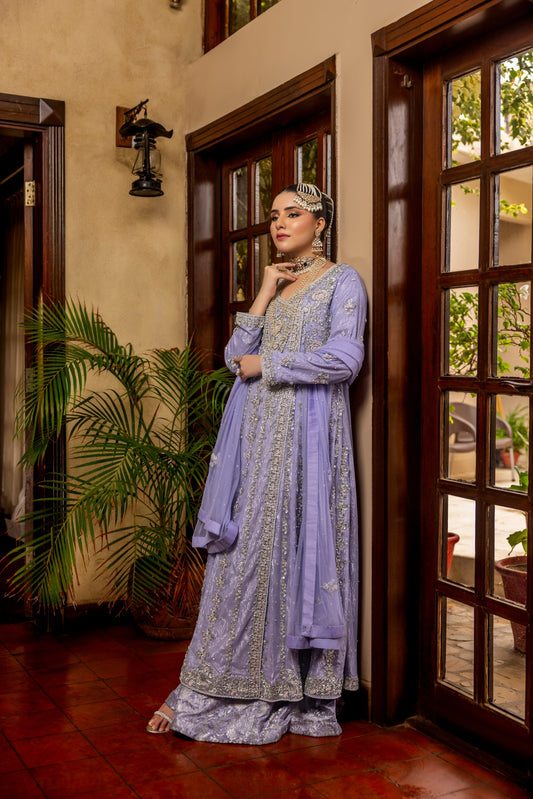 Woman in a light purple traditional bridal maxi outfit standing in a doorway with plants and a door in the background.