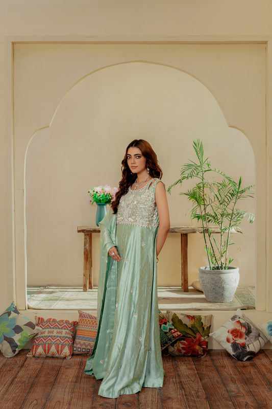 Woman in a light green party wear maxi standing in a room with decorative pillows and plants.